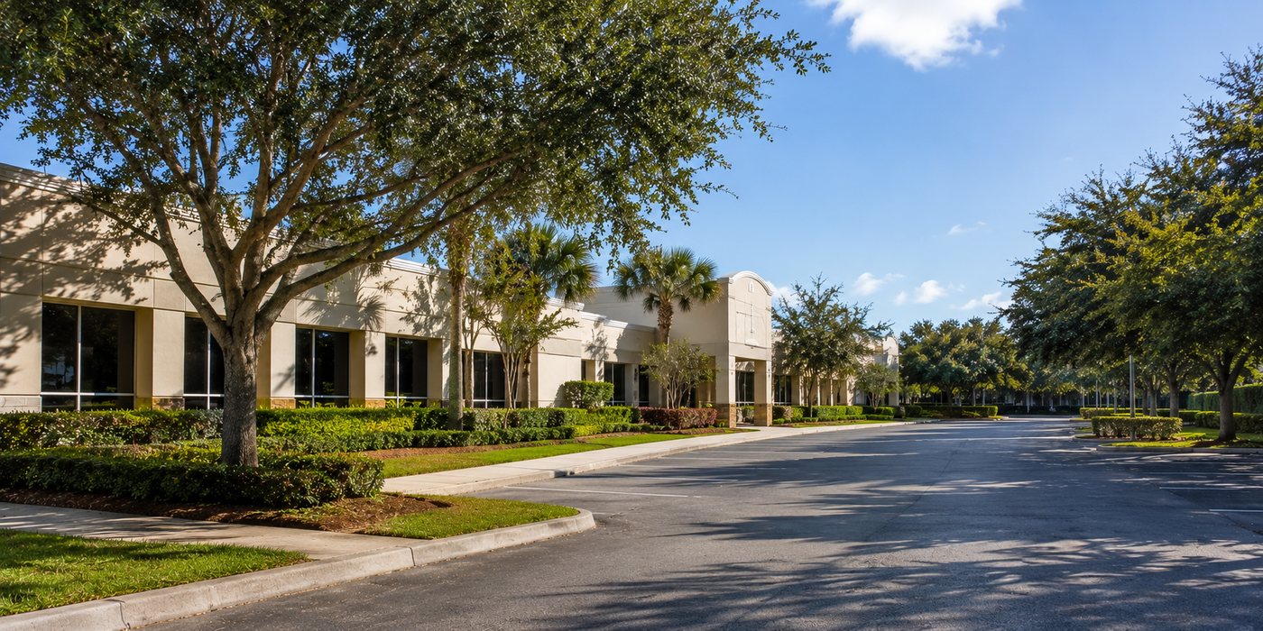 Commercial building with maintained lawn, landscape beds and mature trees beside an empty parking area with no one on site