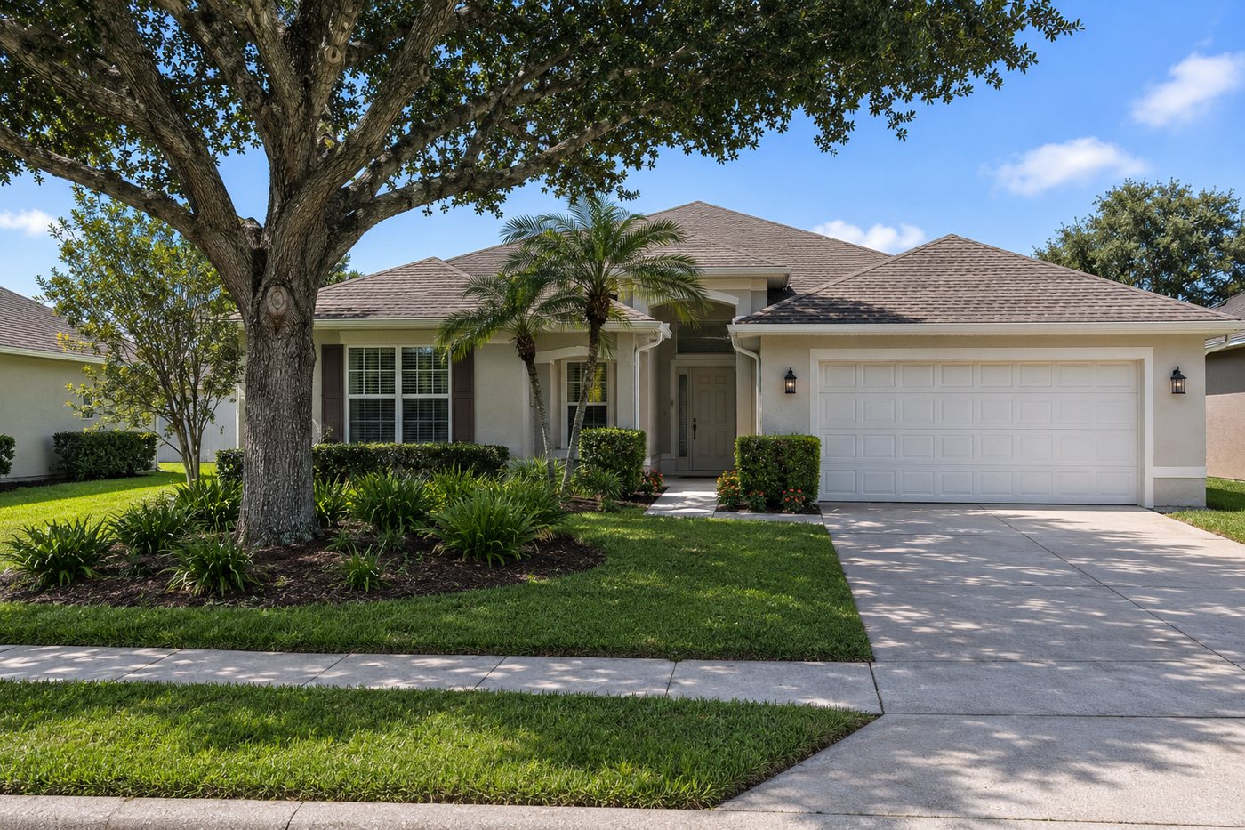 Central Florida home with an empty driveway, mown lawn, landscape beds and a mature oak, with nobody on site